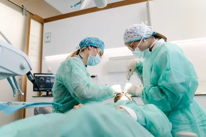 Two surgeons in green scrubs operating on a patient in a dental office.