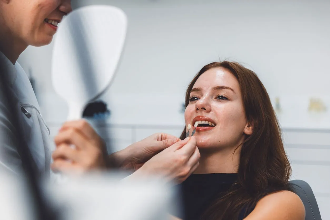 Woman in dentist chair having teeth color matched, held by dentist, with mirror.