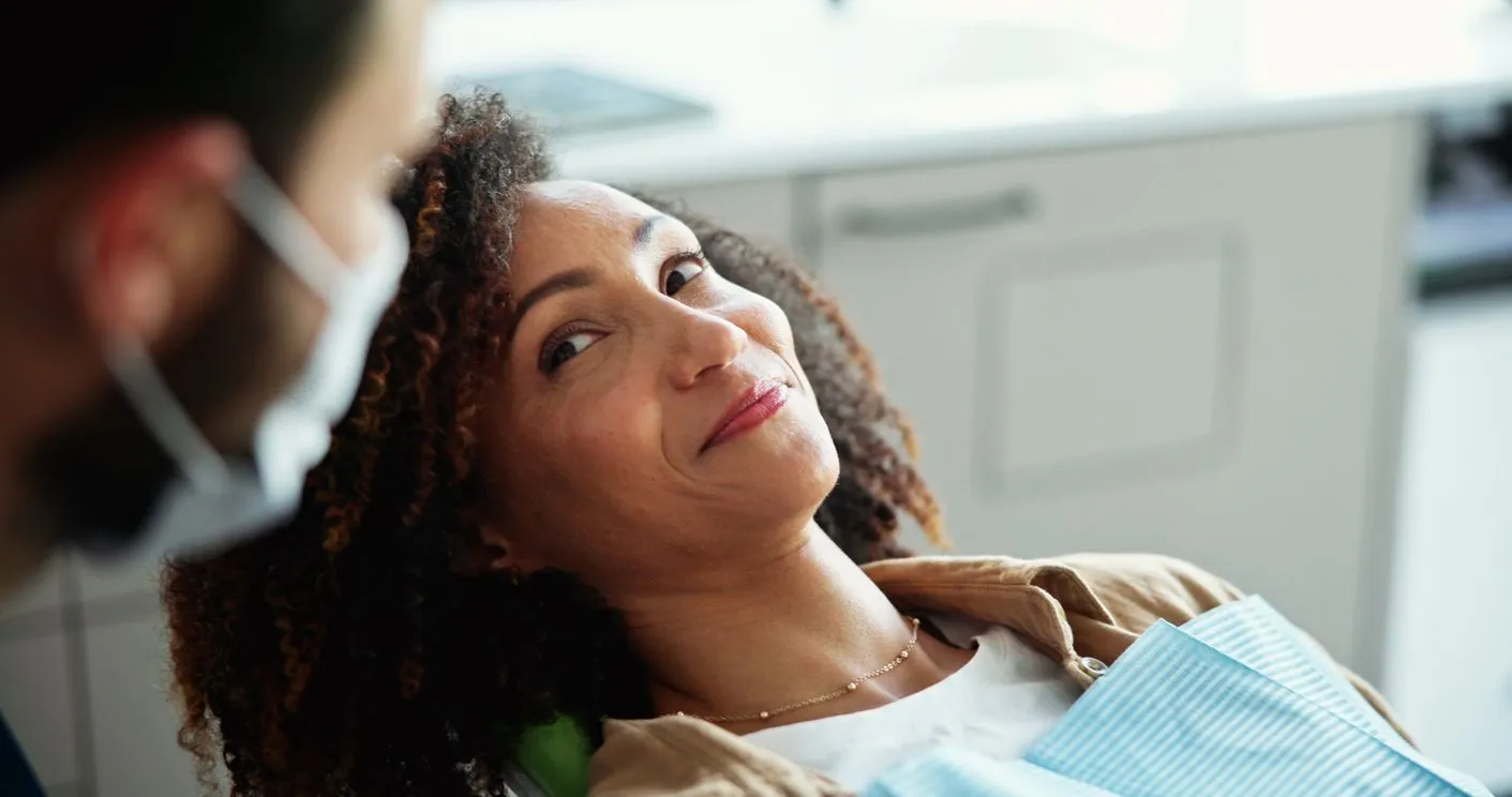 Woman in dental chair looks up at masked dentist.