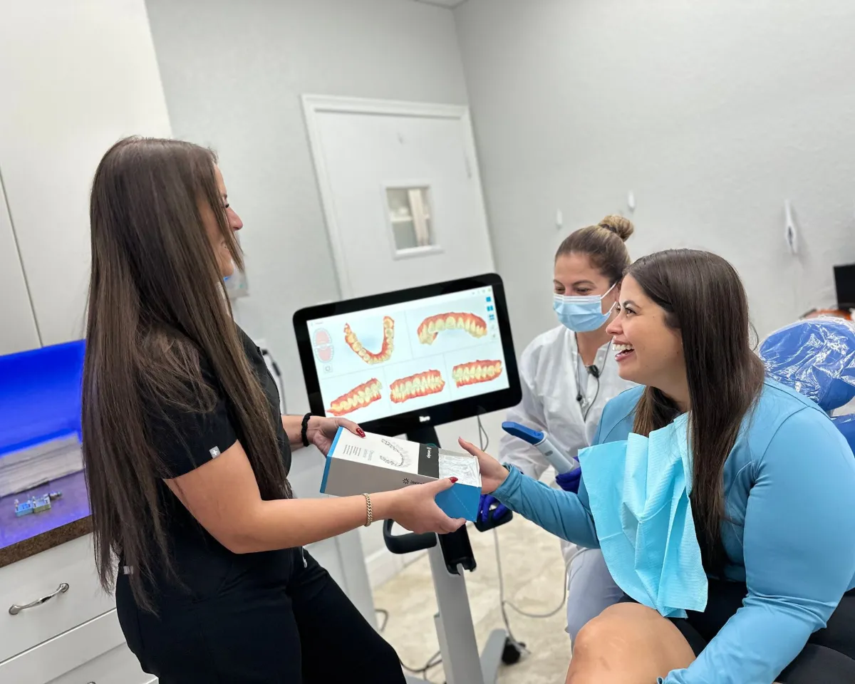 A woman is sitting in a dental chair talking to a dentist and a nurse.
