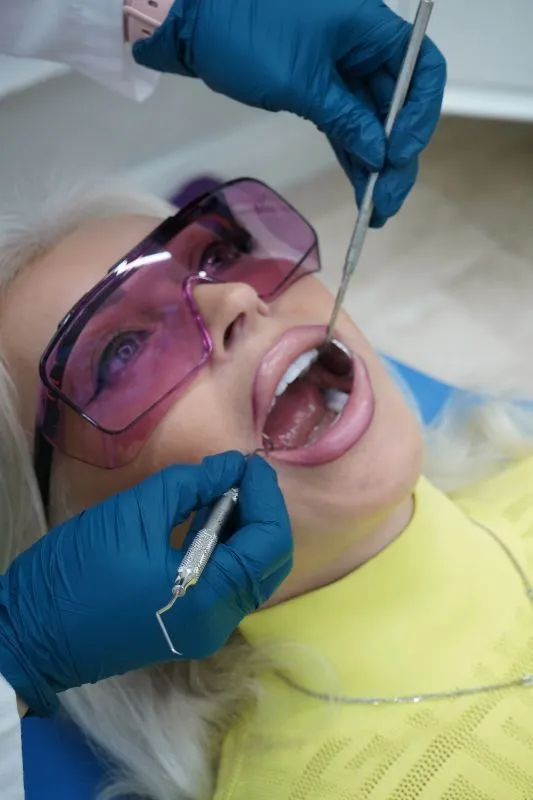 A woman wearing sunglasses is getting her teeth examined by a dentist