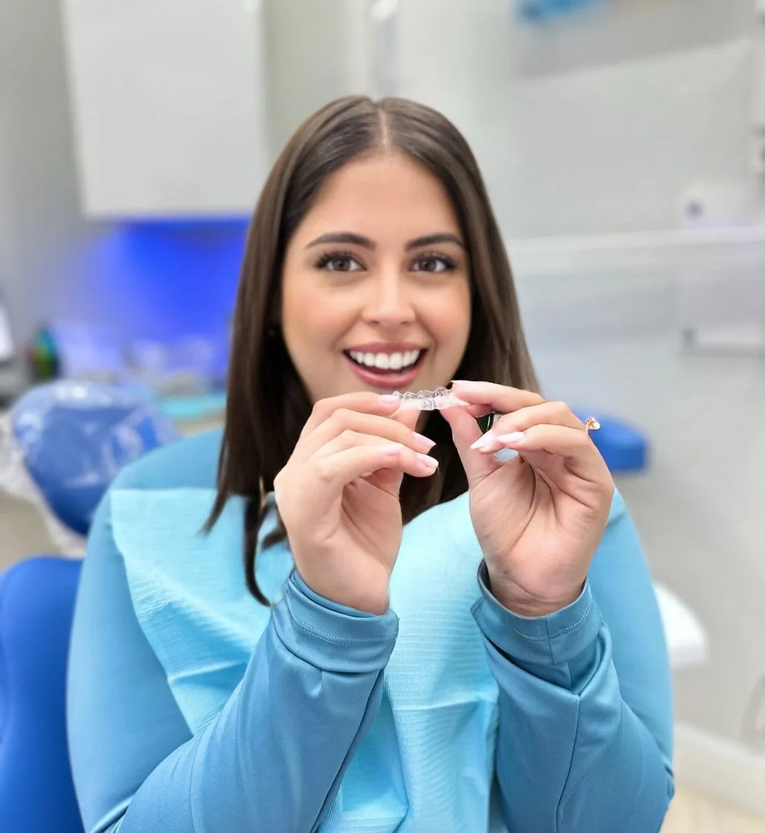 A woman is sitting in a dental chair holding a clear brace.
