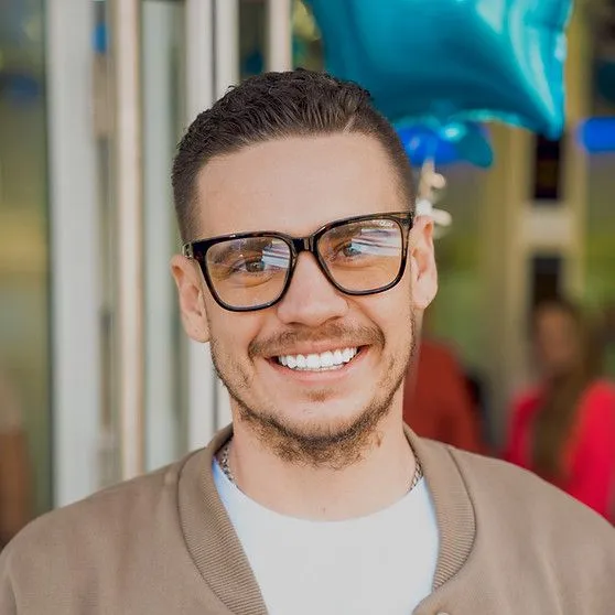A man wearing glasses is smiling in front of a blue balloon.